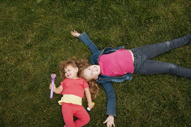 Un retrato de dos hermanas sobre la hierba verde, parque al aire libre - vista superior