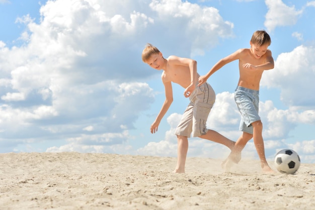 Retrato de dos hermanos jugando al fútbol en la playa en verano
