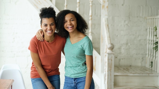 Retrato de dos hermosas chicas afroamericanas riendo y mirando a la cámara en casa