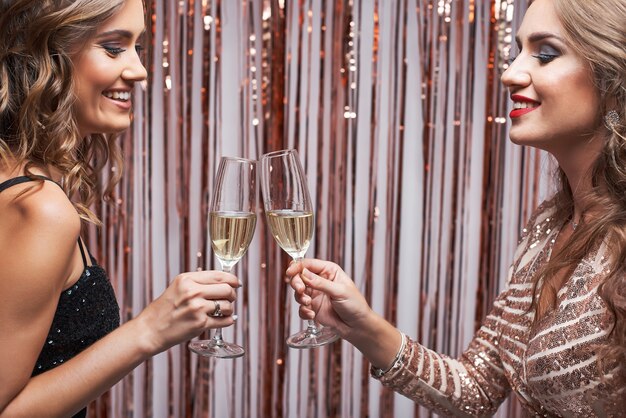 Retrato de dos hermosas mujeres elegantes tintineo copas de champán.