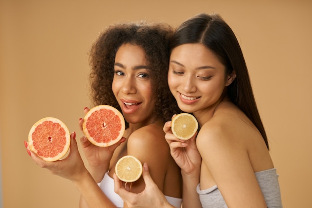 Retrato de dos hermosas mujeres jóvenes de raza mixta sosteniendo pomelo y limón cortado por la mitad