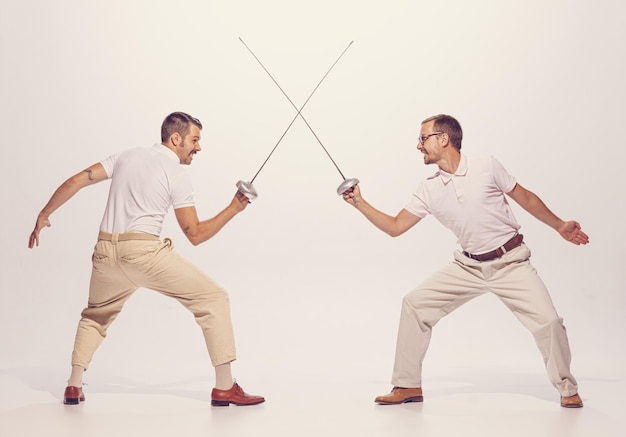 Retrato de dos hombres con traje luchando con espadas aislados sobre el fondo gris del estudio emotivamente