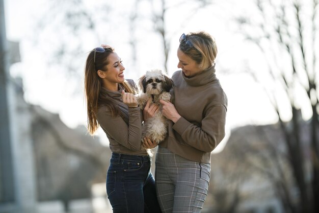 Retrato de dos jóvenes amigas con su perro mascota Shih Tzu en la ciudad.