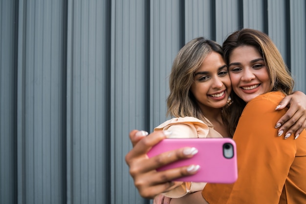 Foto retrato de dos jóvenes amigos sonriendo y tomando un selfie con su teléfono móvil al aire libre. concepto urbano.