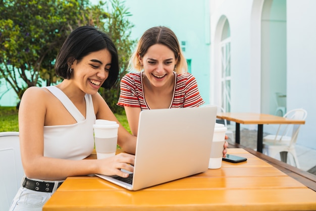 Retrato de dos jóvenes amigos usando una computadora portátil en la cafetería.