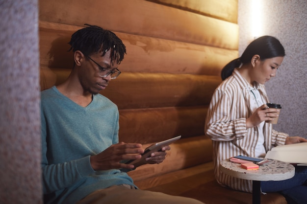 Retrato de dos jóvenes disfrutando de un descanso en el café se centran en el hombre afroamericano moderno con smartphone en café