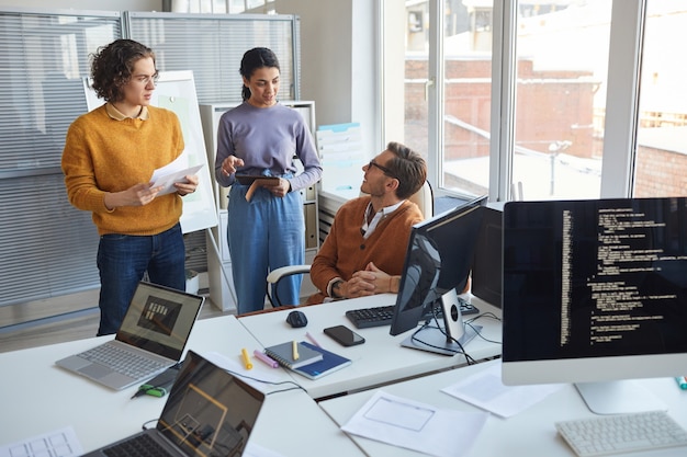 Retrato de dos jóvenes hablando con el gerente masculino mientras se discute el proyecto de desarrollo de software en la oficina moderna, espacio de copia