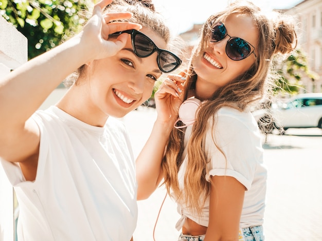 Retrato de dos jóvenes hermosas mujeres hipster sonrientes en ropa de camiseta blanca de verano de moda