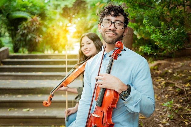 Retrato de dos jóvenes violistas sentados afuera Hombre y mujer violinista sentados en las escaleras Concepto de dos jóvenes violinistas Dos jóvenes violinistas sentados al aire libre mirando a la cámara