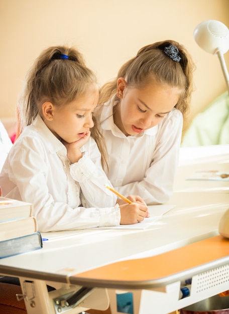 Retrato de dos lindas alumnas escribiendo en libros de texto en el escritorio