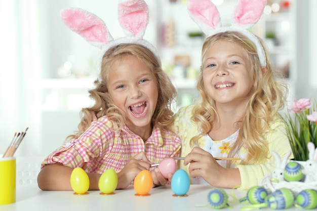 Retrato de dos lindas hermanas con orejas de conejo y pintando huevos de Pascua