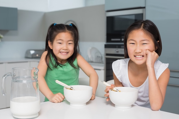 Retrato de dos muchachas sonrientes que se sientan con los cuencos en cocina