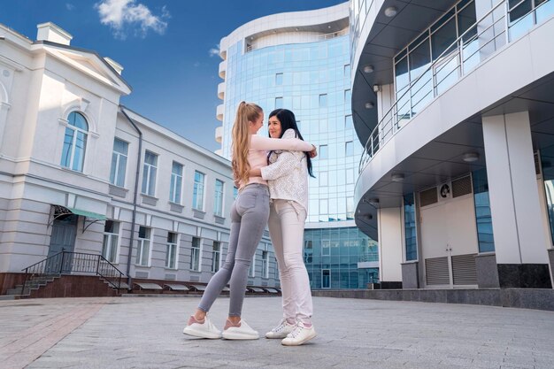 Retrato de dos mujeres abrazadas junto a un hermoso edificio de cristal