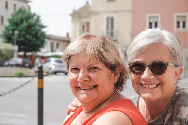 Retrato de dos mujeres caucásicas con expresión positiva se abrazan posando para un retrato familiar sentado al aire libre en la ciudad Personas emociones y amistad