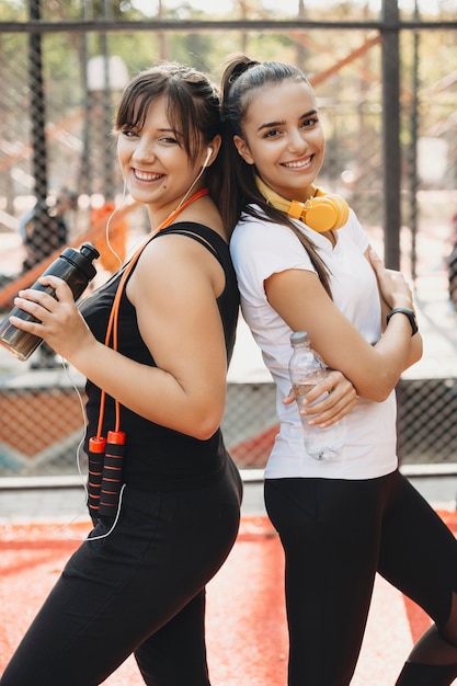 Foto retrato de dos mujeres encantadoras después de hacer ejercicios para perder peso por la mañana agua potable al aire libre y riendo.