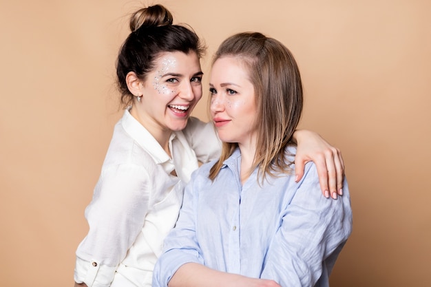 Retrato de dos mujeres felices sonriendo con los brazos cruzados aislado sobre pared beige