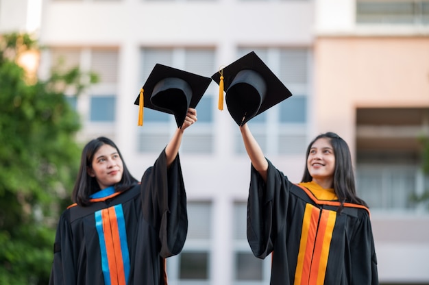 Retrato Dos mujeres graduadas, graduadas universitarias, felizmente sosteniendo sus sombreros al frente.