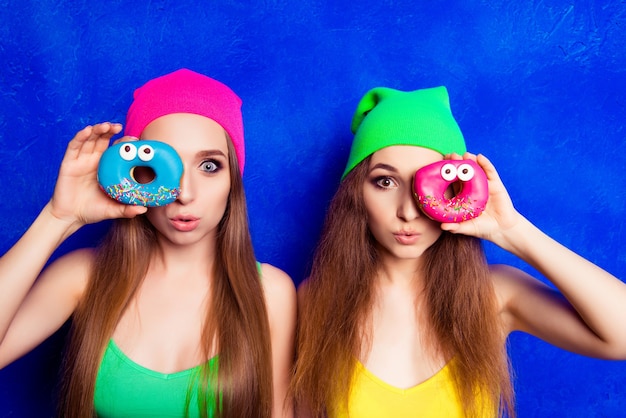 Retrato de dos mujeres haciendo pucheros y sosteniendo donuts cerca del ojo