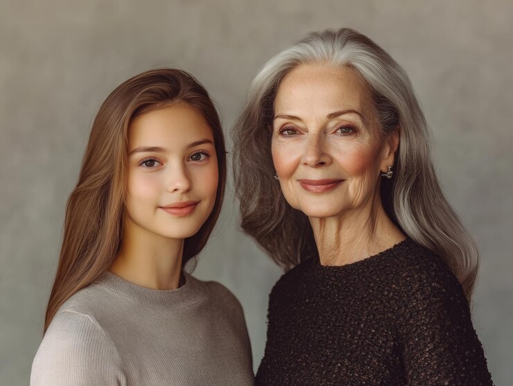 Retrato de dos mujeres hermosas una más joven y otra más vieja de pie una al lado de la otra sonriendo con un fondo neutro suave