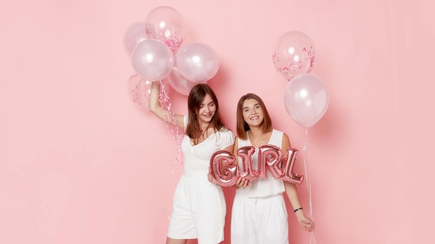 Retrato de dos mujeres jóvenes felices vestidas de blanco sosteniendo globos sobre fondo rosa Espacio para texto