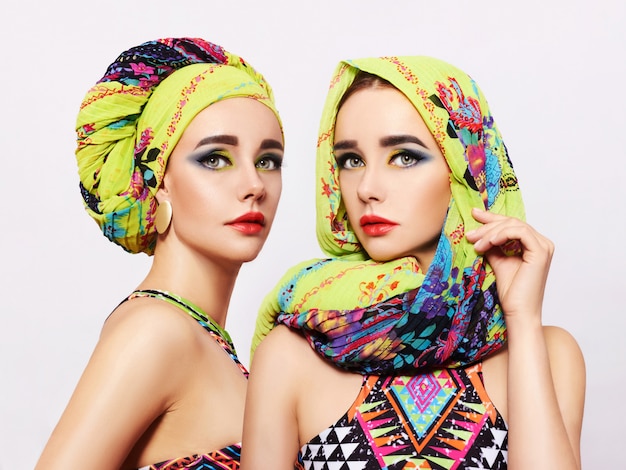 Retrato de dos mujeres jóvenes con maquillaje brillante y un pañuelo de moda