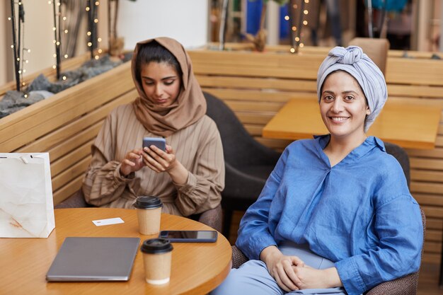 Retrato de dos mujeres jóvenes de Oriente Medio relajándose en la cafetería mientras disfruta de las compras en el centro comercial, espacio de copia