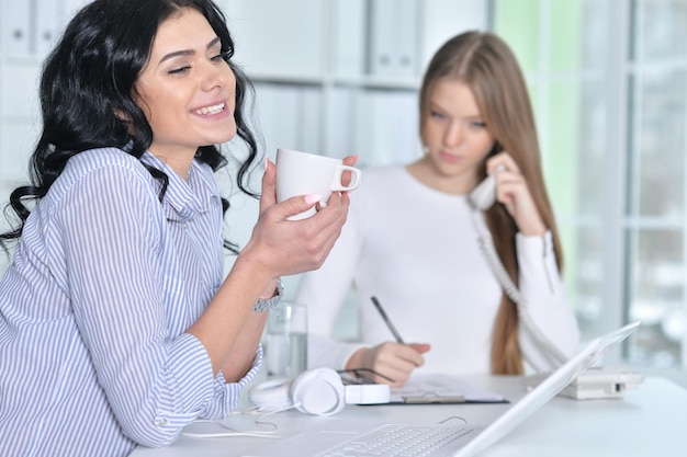 retrato, de, dos, mujeres jóvenes, trabajando, en, oficina, con, computador portatil