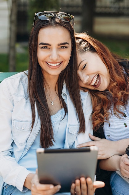 Retrato de dos mujeres mientras uno sostiene una tableta sonriendo cuando otro está apoyando su cabeza en el hombro de su novia riendo