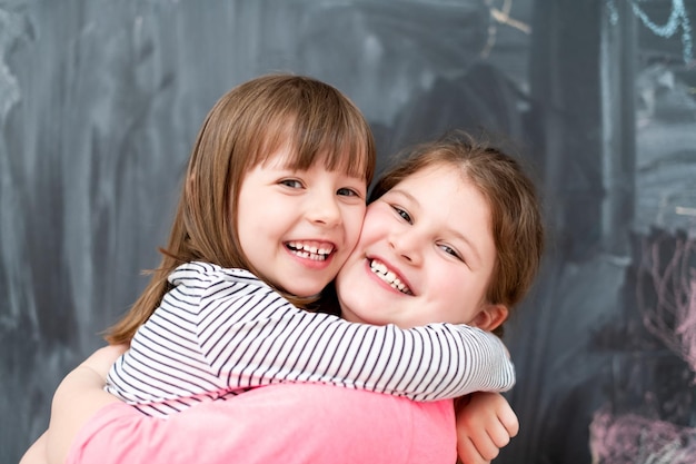 retrato de dos niñas felices y lindas abrazándose mientras se divierten frente a una pizarra negra