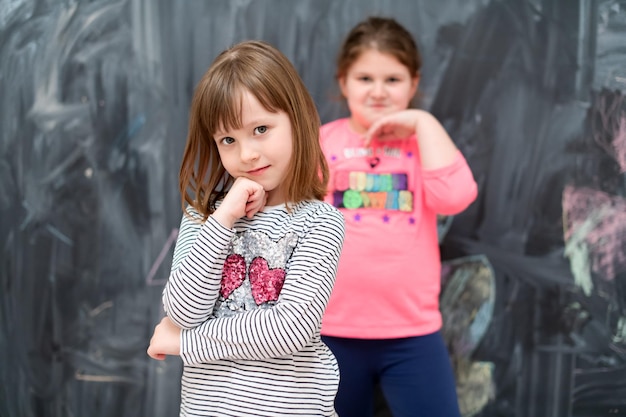 retrato de dos niñas felices y lindas paradas frente a una pizarra negra