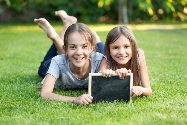 Retrato de dos niñas felices tumbado en el césped con pizarra