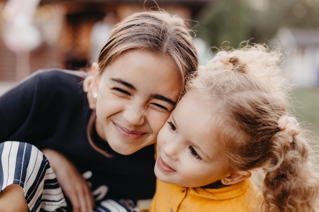 Retrato de dos niñas lindas donde una niña rizada más pequeña abraza a una niña mayor con pecas en la cara