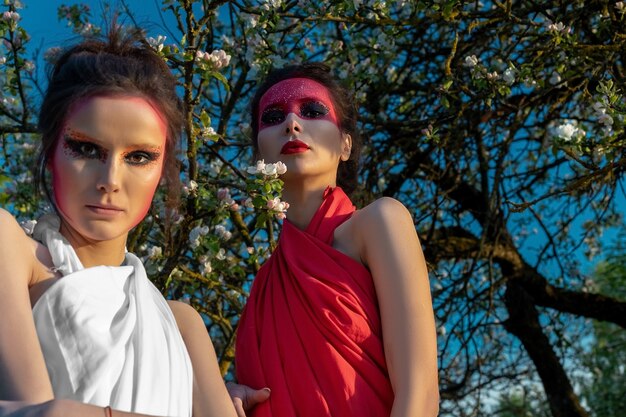 Retrato de dos niñas con maquillaje creativo en el fondo de un manzano en flor