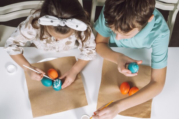 Retrato dos niños niña niño hermanos pintando huevos de Pascua multicolores en pincel de cocina Vista superior