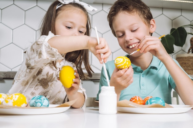 Retrato de dos niños sonrientes y alegres, una niña pequeña, pintando huevos de Pascua, mesa de cocina con pinceles