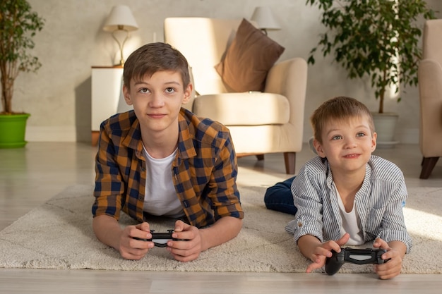 Foto retrato de dos niños tirados en el suelo en una habitación jugando videojuegos con joysticks