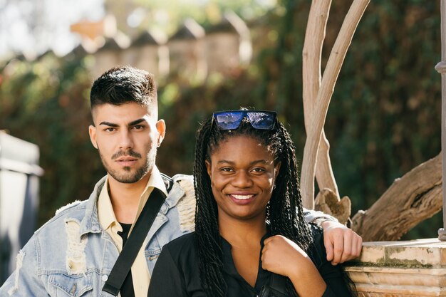 Retrato de dos personas multiétnicas sonriendo a la cámara mientras está de pie en un parque