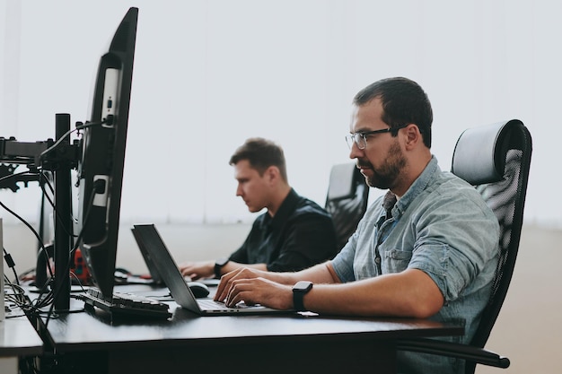 Foto retrato de dos programadores masculinos profesionales que trabajan en computadoras en diversas oficinas desarrollo de tecnologías de ti modernas de aplicaciones de programas de inteligencia artificial y concepto de videojuegos