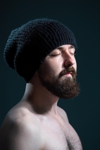 Retrato dramático de um cara barbudo em um chapéu de malha preto em um fundo escuro