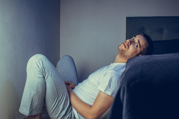 Retrato dramático do estilo de vida de um cara bonito na casa dos 30 e 40 anos, sentado tristemente na cama, sentindo-se ansioso e sofrendo de depressão Homem atraente deprimido e chateado no quarto de casa