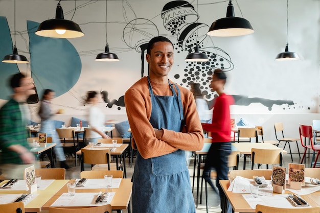 Retrato de un dueño o camarero sonriente en un café con empleados borrosos irreconocibles moviéndose