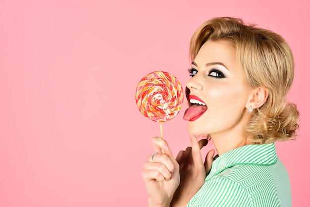 Retrato de dulce niña con piruleta sobre fondo rosa cerca de estilo pin up sonriendo