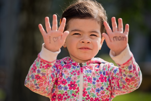 Retrato de una dulce niña que dice "Amo a mamá" en sus palmas