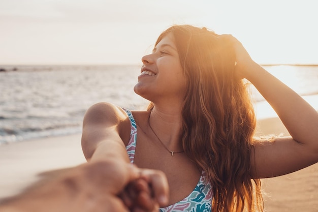 Foto retrato e close-up de jovem segurando a mão do namorado andando na praia sorrindo e se divertindo juntos homem seguindo namorada para a água do mar desfrutando