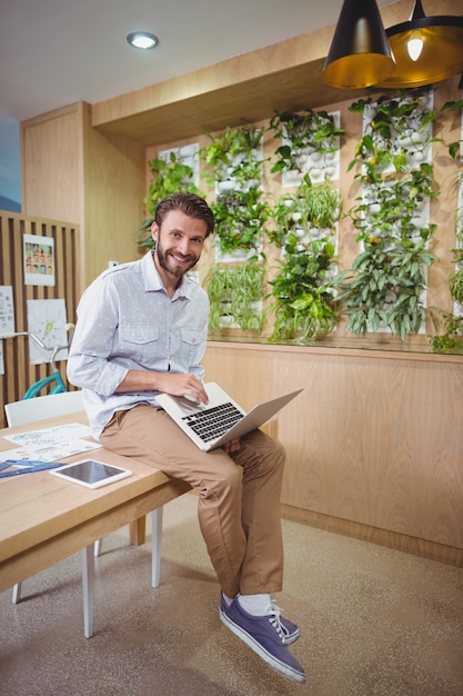 Retrato ejecutivo de negocios masculino sentado en el escritorio y usando laptop