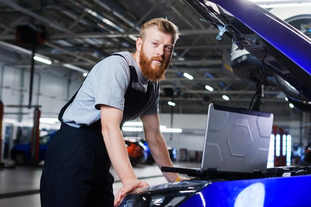 Retrato de un electricista automotriz profesional que diagnostica errores de camión usando una computadora portátil en el contexto de una estación de servicio