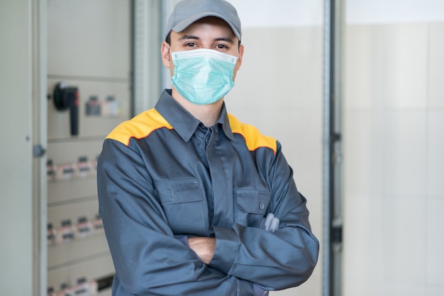 Foto retrato de un electricista frente a un panel eléctrico industrial en una fábrica con una máscara