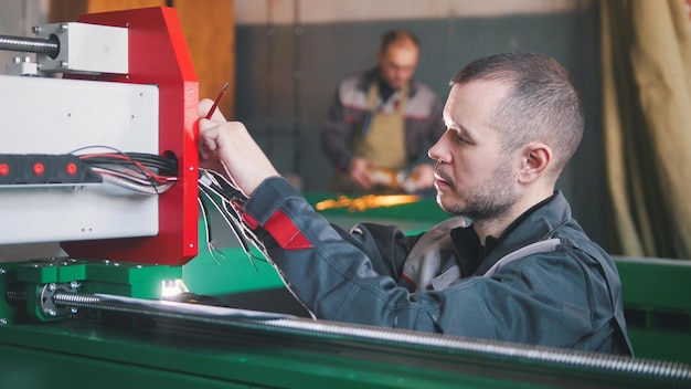 Retrato de electricista en overoles está trabajando con panel de energía y equipo de maquinaria en la planta