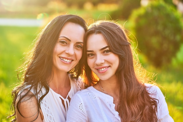 Retrato de elegante atractivo sonriente alegre feliz madre e hija juntos en un parque al aire libre al atardecer con luz suave