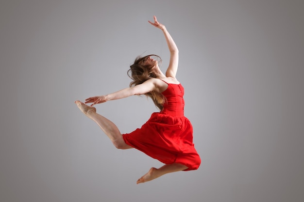 Retrato de una elegante bailarina vestida de rojo saltando en el aire